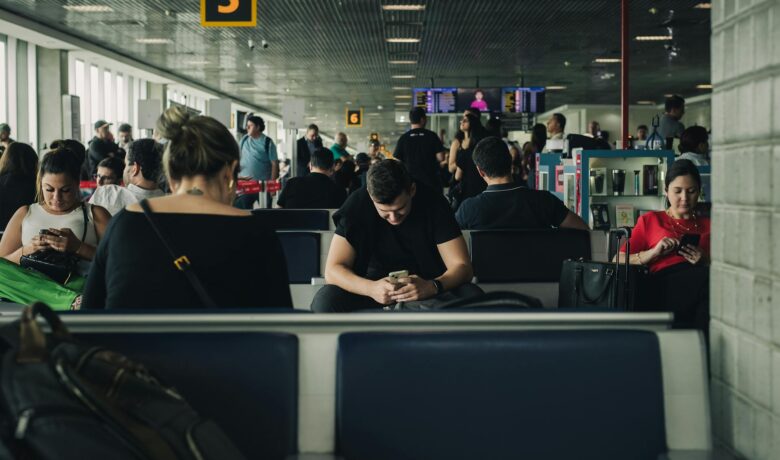 Sala de embarque cheia, passageiros usando smartphones enquanto aguardam voos.