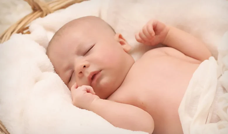 Bebê recém-nascido dormindo em um cesto, envolto em um tecido branco.